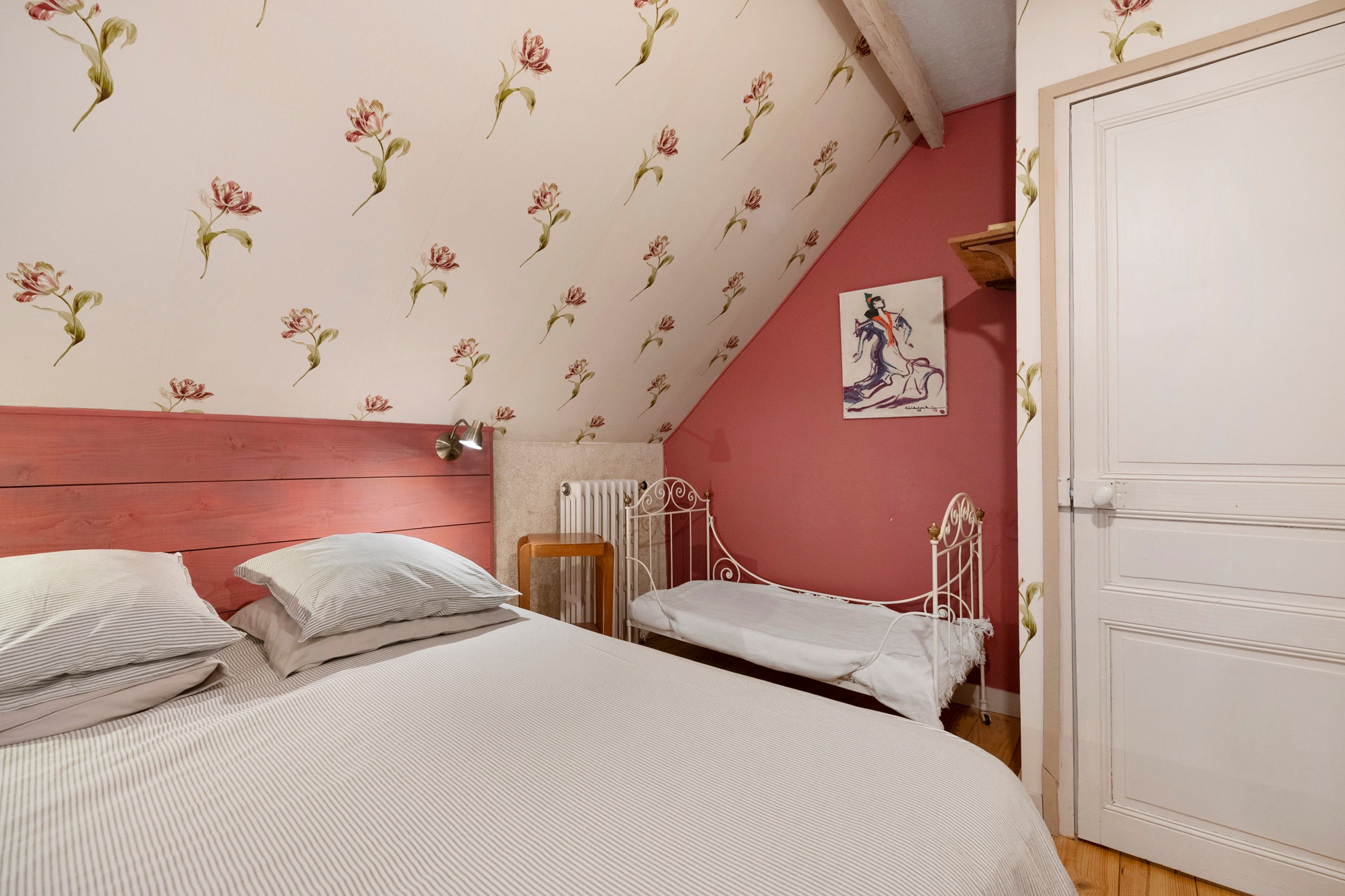 A bedroom with a sloped ceiling, a bed with two pillows, a radiator, and a door.