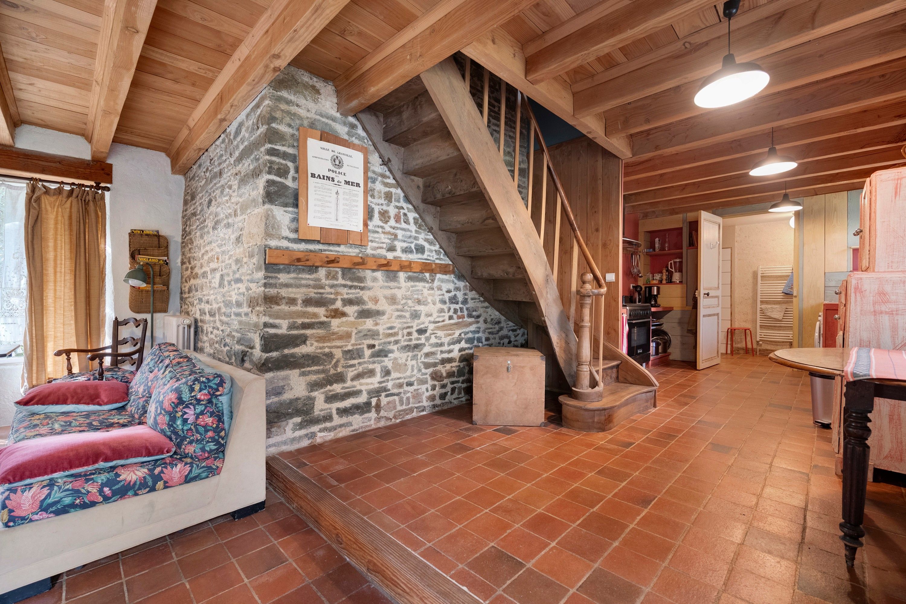 Un interno rustico con parete in pietra, scala in legno e un'accogliente area salotto con cuscino floreale.