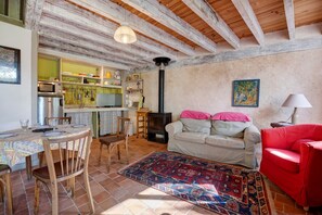 A cozy living room with a fireplace, a dining area with a table set for two, and a kitchen with wooden shelves. - BiâO Petitgîte holiday home with terrace, shared garden, and Wi-Fi (Bretteville-sur-Ay)