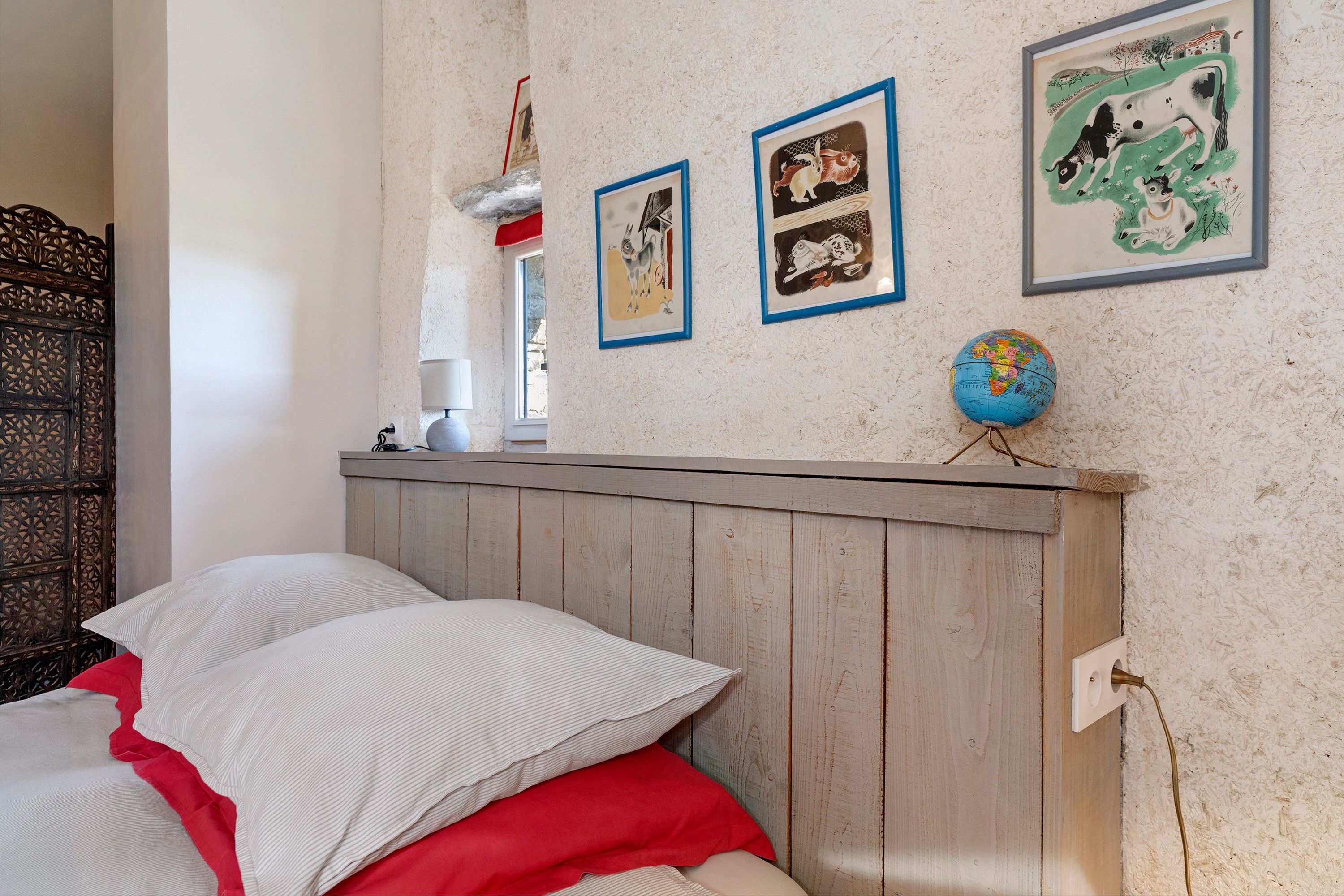 Ein Schlafzimmer mit einem Holz-Kopfteil, einem Bett mit weißer und roter Bettwäsche, einer Lampe und drei gerahmten Bildern an der Wand.