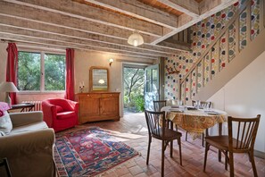 A room with a wooden ceiling, a dining table set with chairs, a red armchair, a cabinet, and a patterned rug. - BiâO Petitgîte holiday home with terrace, shared garden, and Wi-Fi (Bretteville-sur-Ay)