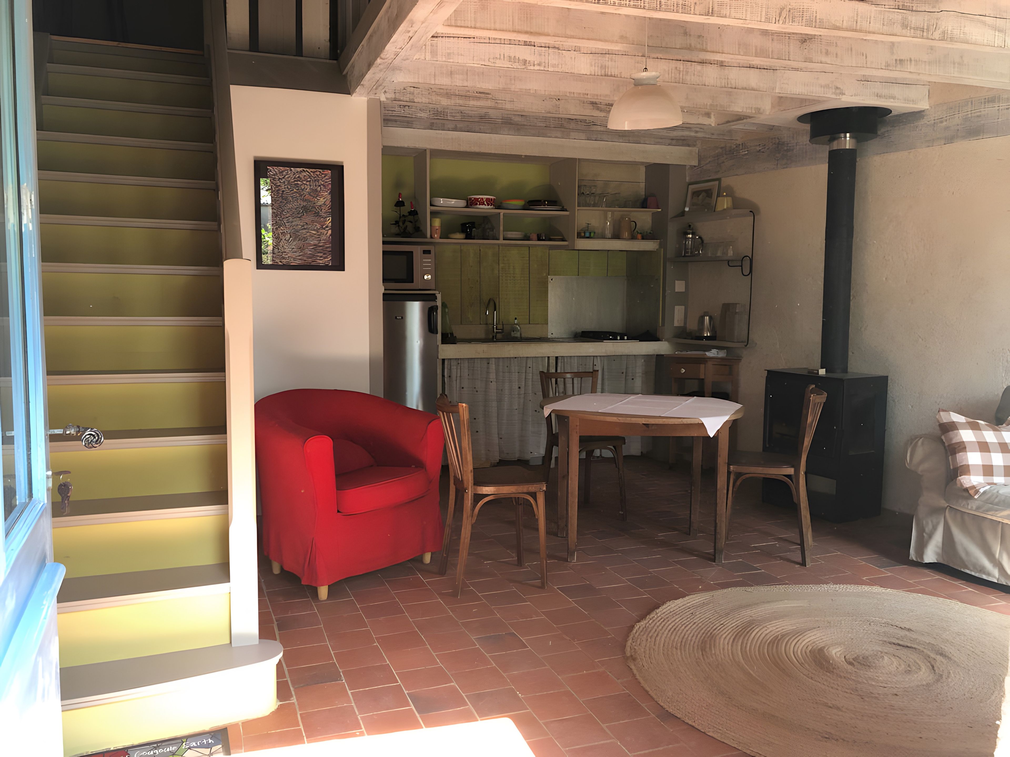 A compact kitchen with a dining area, a red chair, and a round rug.