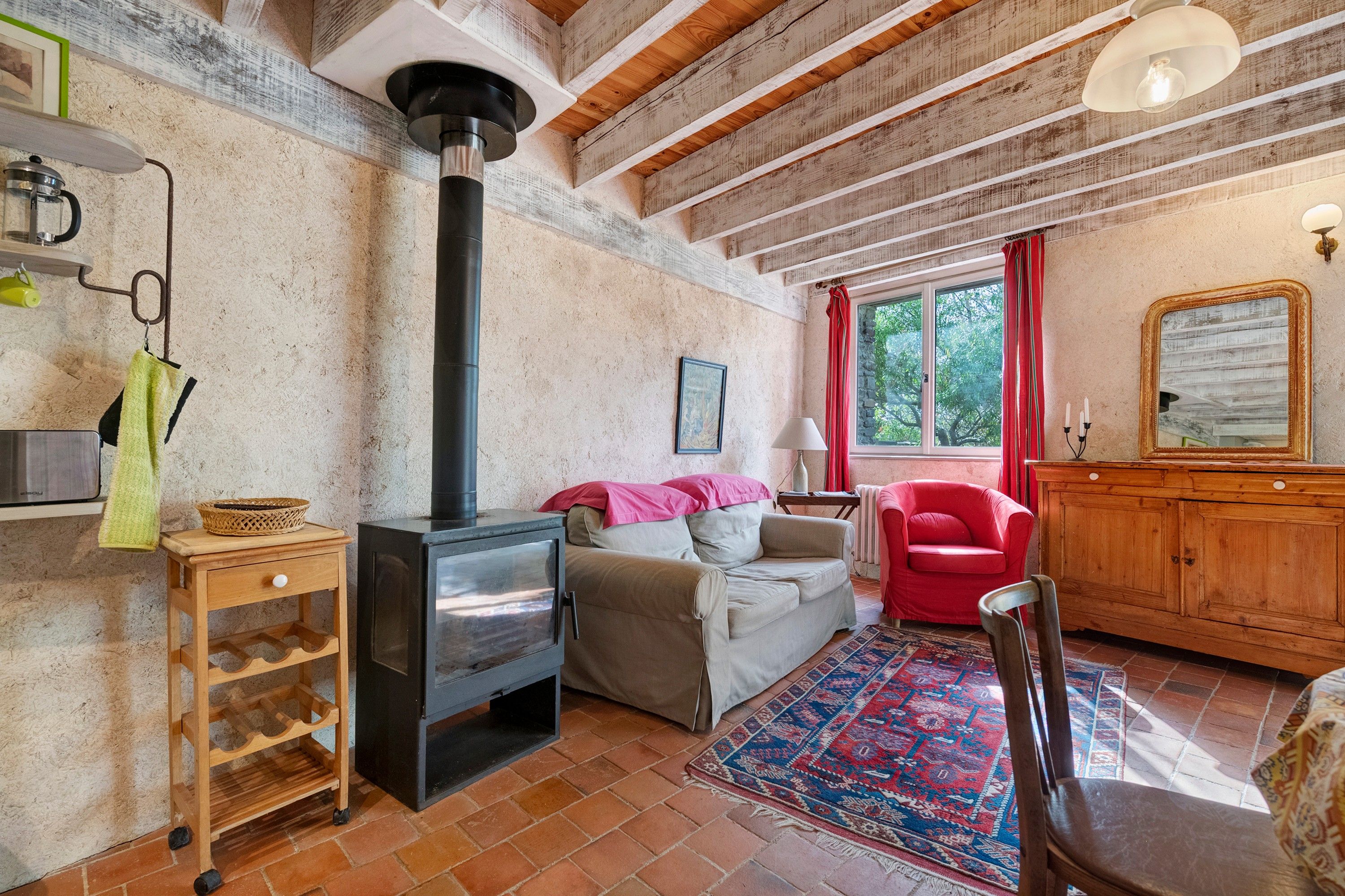 Un salon chaleureux avec une cheminée, un canapé, un fauteuil rouge et un meuble en bois.