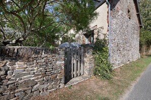 A stone building with a wooden gate, surrounded by greenery and a clear sky. - BiâO Petitgîte holiday home with terrace, shared garden, and Wi-Fi (Bretteville-sur-Ay)