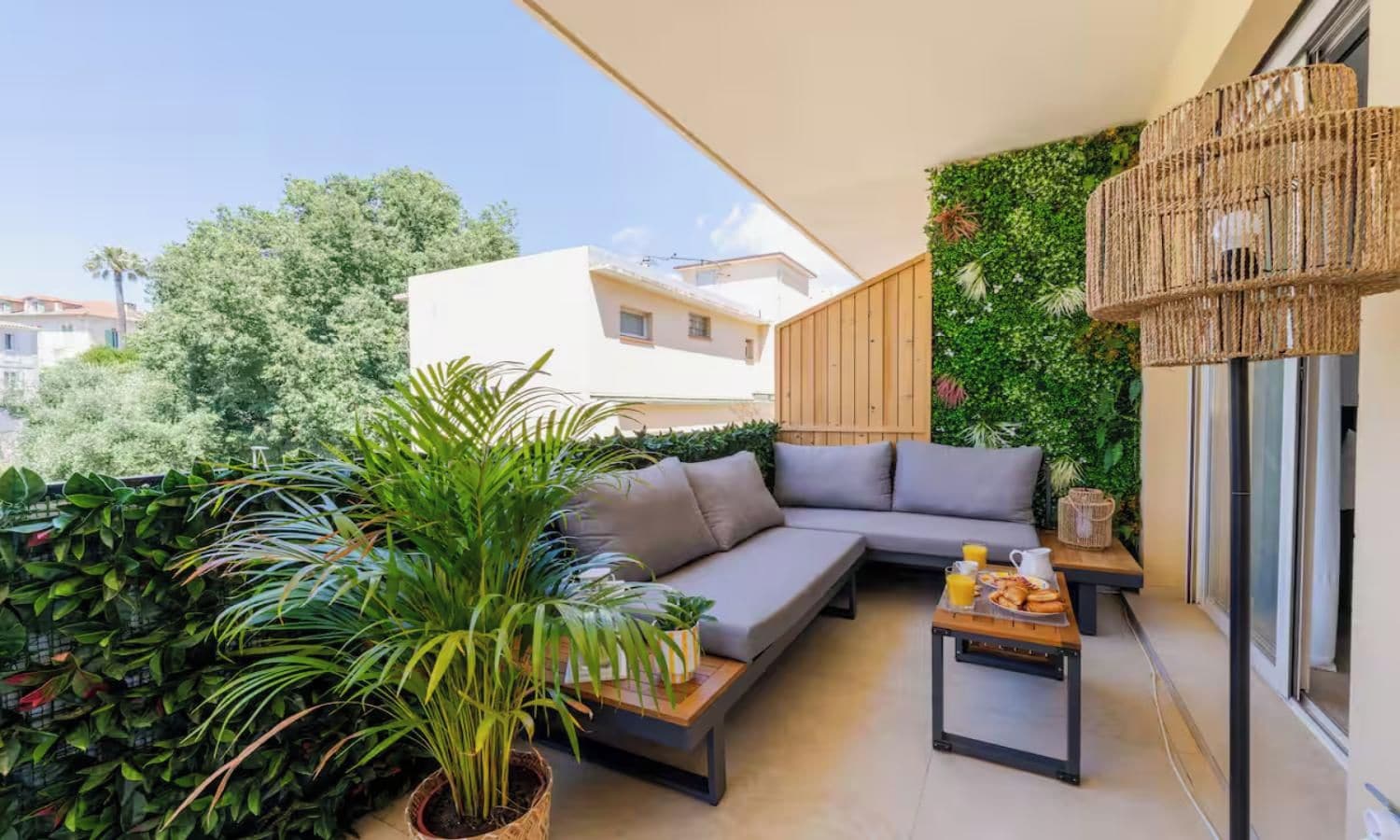 A balcony with a grey sofa, a small table with a tray of food, and lush greenery.