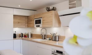 A modern kitchen with wooden cabinets, a stainless steel sink, and a microwave. - Modern Cannes Apartment with Sunny Terrace & Private Parking (Cannes)