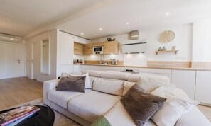 A modern living room with a sofa, a coffee table, and a kitchen area with a microwave and cabinets. - Modern Cannes Apartment with Sunny Terrace & Private Parking (Cannes)