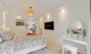 A bedroom with a bed, a bedside table, a mirror, a TV, and a door leading to a bathroom. - Modern Cannes Apartment with Sunny Terrace & Private Parking (Cannes)