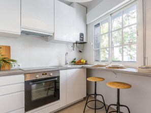 A modern kitchen with white cabinets, a built-in oven, a window with a view, and two stools. - Cozy 2-Bed Apartment in Málaga with Modern Amenities and Central Location (Málaga)