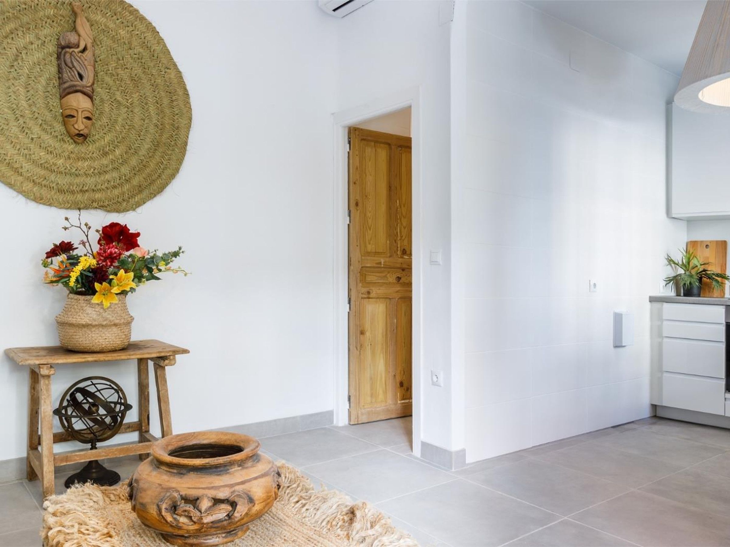 A modern interior with a wooden door, a white wall, and a kitchen area with white cabinets.