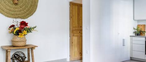 A modern interior with a wooden door, a white wall, and a kitchen area with white cabinets.
