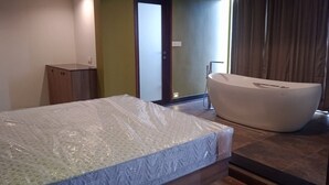 A bedroom with a mattress, a wooden cabinet, a bathtub, and a door leading to another room. - Soul by Araiya, Paithalmala, A Vihaara Resort & Spa (Kannur)
