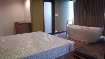 Un dormitorio con un colchón, un armario de madera, una bañera y una puerta que da a otra habitación.