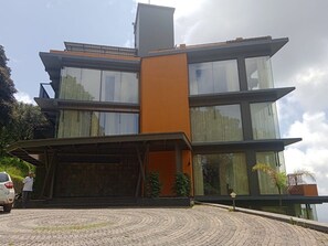 A modern multi-story building with a flat roof, large windows, and a prominent orange accent wall.