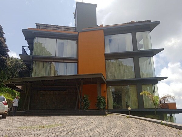 A modern multi-story building with a flat roof, large windows, and a prominent orange accent wall.