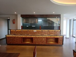 A reception area with a counter, seating, and a staircase in the background. - Soul by Araiya, Paithalmala, A Vihaara Resort & Spa (Kannur)