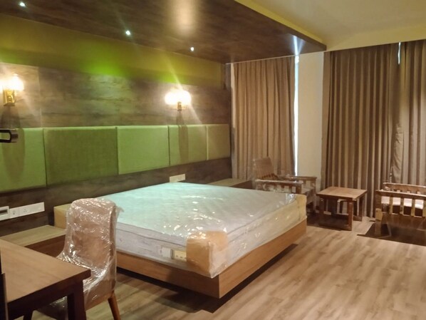 A hotel room with a wooden bed, a wooden desk, a chair, a small table, and a wall-mounted lamp.