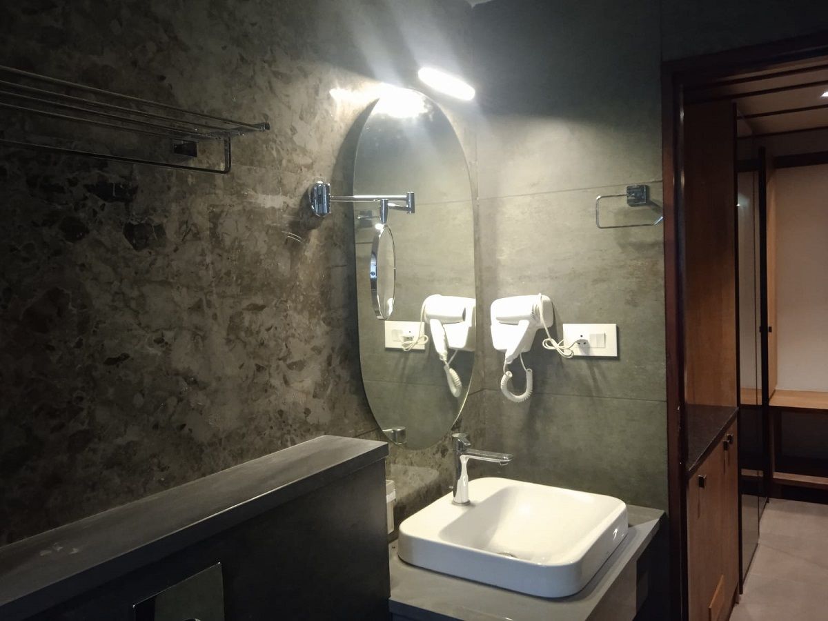 A bathroom with a rectangular sink, a mirror, and two hair dryers mounted on the wall.