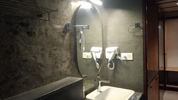 A bathroom with a rectangular sink, a mirror, and two hair dryers mounted on the wall.