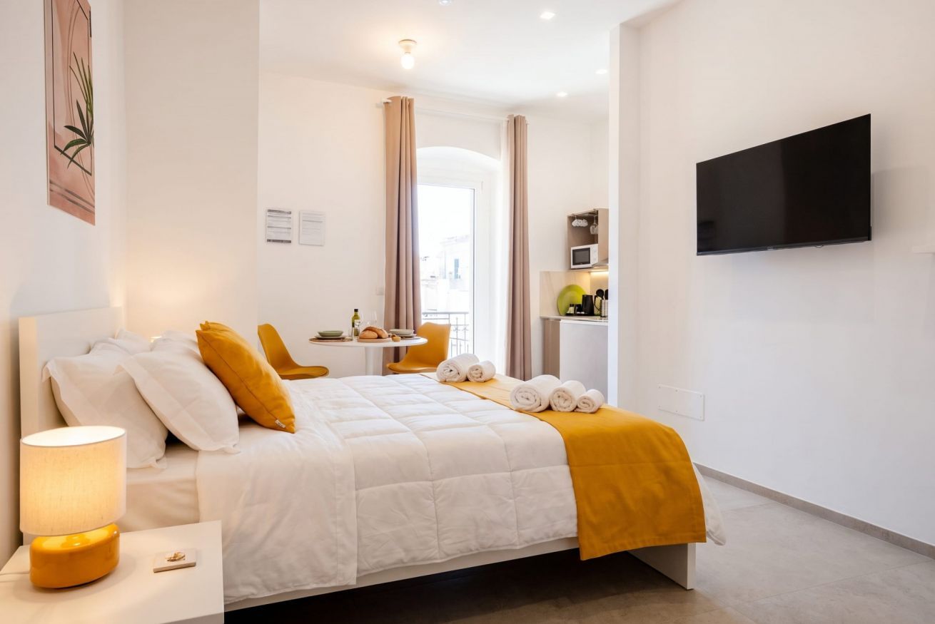 Een hotelkamer met een bed, een nachtkastje met een lamp, een flatscreen televisie aan de muur en een klein tafeltje met een stoel.