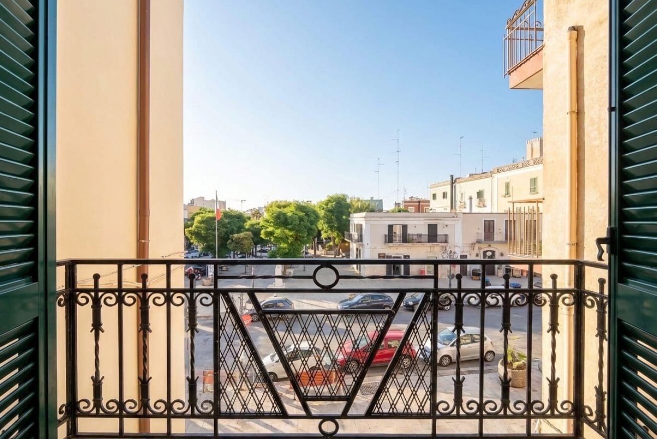 Ein Balkon mit schmiedeeisernem Geländer mit Blick auf eine Straße mit geparkten Autos und Gebäuden.