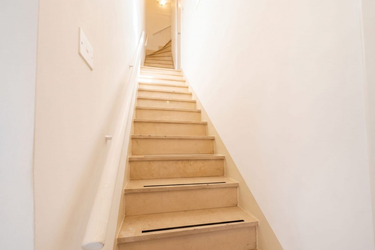 A narrow, white-walled stairway leading to a landing.