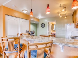 Una cocina con encimera de mármol, sillas de madera e iluminación colgante.