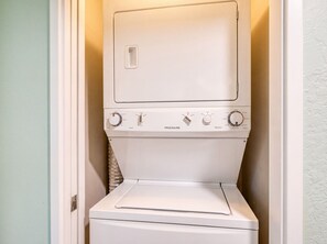 Eine weiße Waschmaschine mit Bedienfeld, die in einer Ecke eines Raumes mit einer hellgrünen Wand steht.