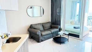 A modern living room with a sofa, a small round table, a mirror, and a large window with curtains. - Artisan Ratchada Condo Bangkok (Krung Thep Maha Nakhon)