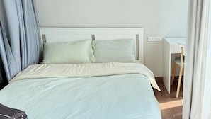 A bed with a white headboard, a desk with a chair, and a curtain partially drawn. - Artisan Ratchada Condo Bangkok (Krung Thep Maha Nakhon)