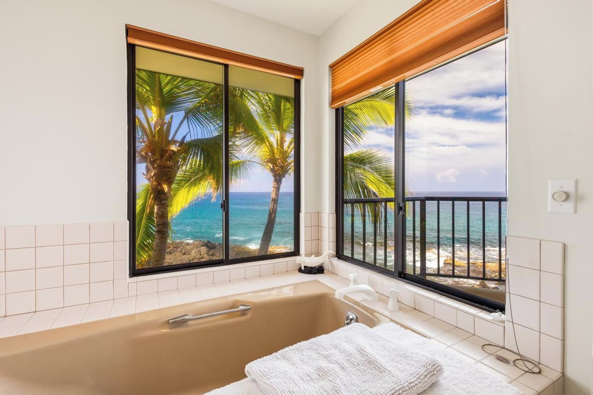 A bathroom with a bathtub, a towel, and a view of the ocean through large windows.