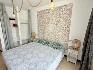 A bedroom with a bed, two bedside tables, a wall tapestry, and a hanging light fixture. - Apartment 'CasaMar El Cotillo' with Sea View, Wi-Fi and Air Conditioning (El Cotillo)
