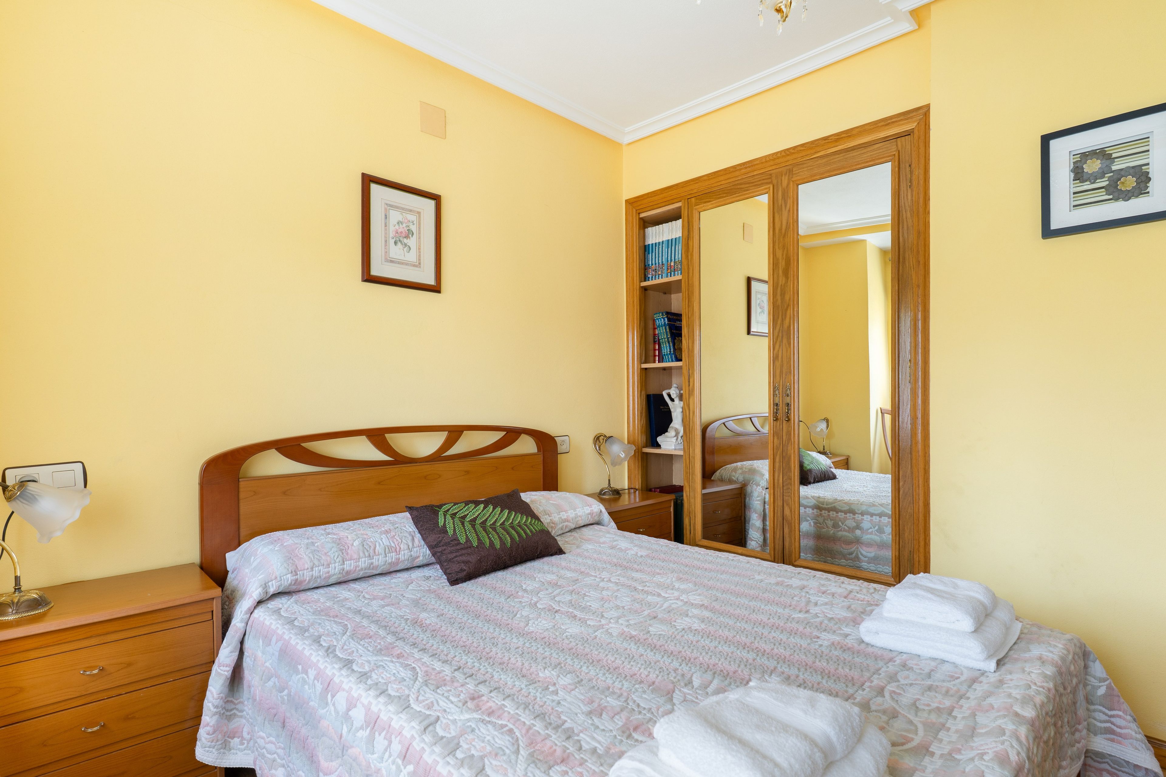 Un dormitorio con cama, mesitas de noche, una lámpara, un espejo y un armario.