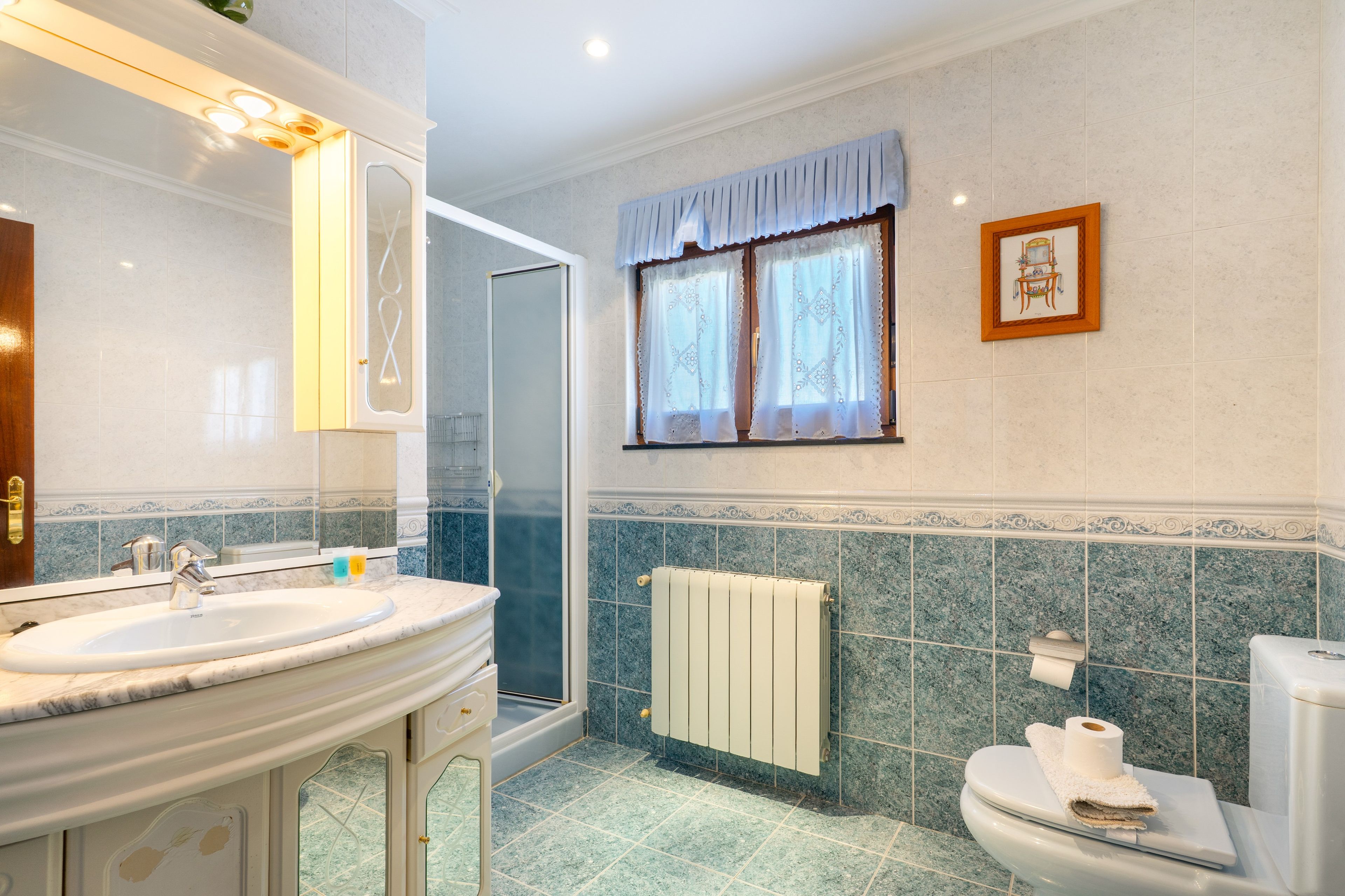 Un bagno con doppio lavandino, doccia, toilette e finestra con tende.