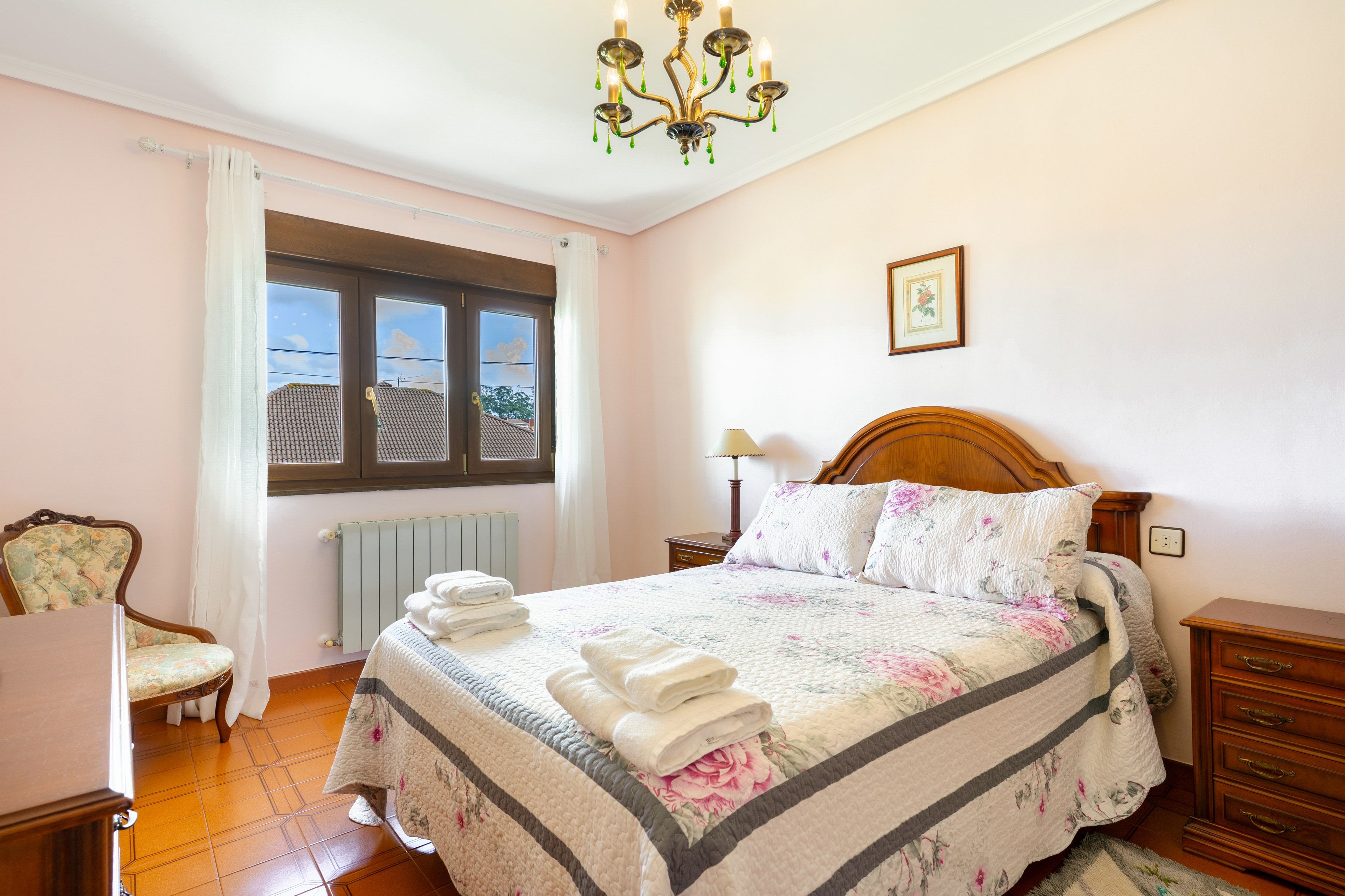 Un dormitorio con cama, una silla, una mesita de noche, una lámpara, un radiador y una ventana.