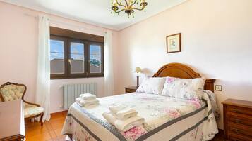 Un dormitorio con cama, una silla, una mesita de noche, una lámpara, un radiador y una ventana.
