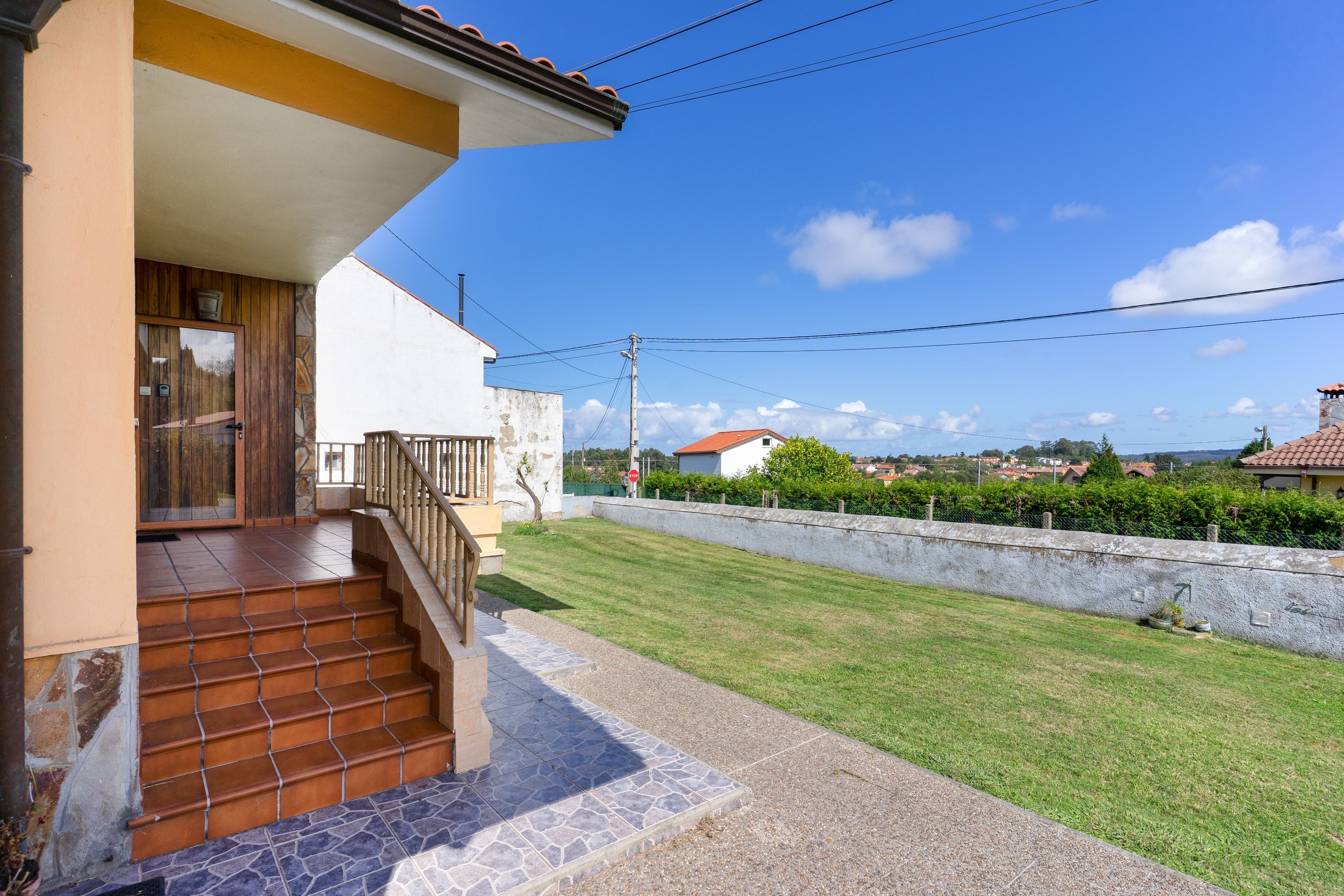 Um imóvel residencial com escadaria que leva a uma porta de madeira, área pavimentada e vista para um bairro com casas e vegetação.