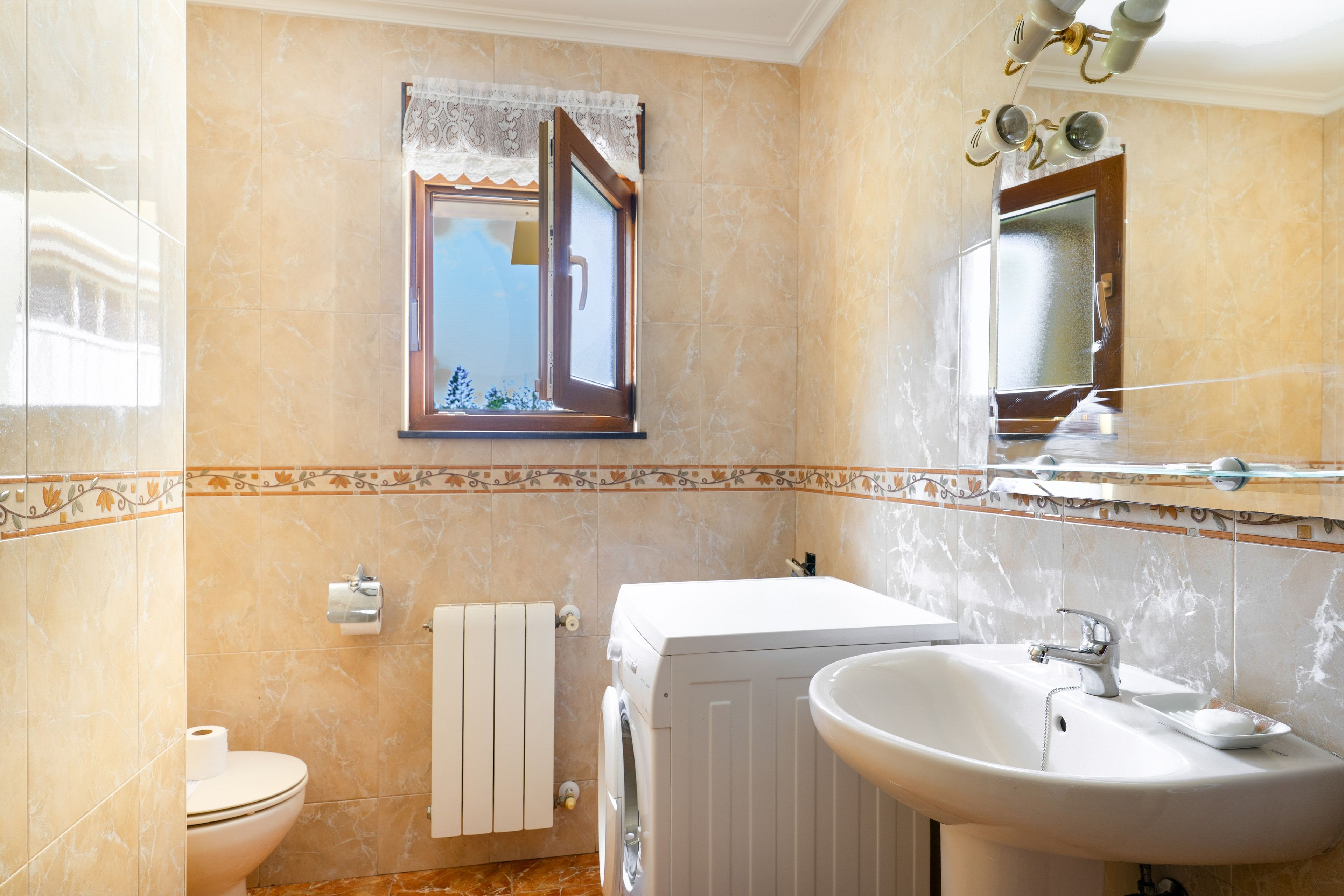 Un baño con inodoro, lavadora, lavabo y espejo.