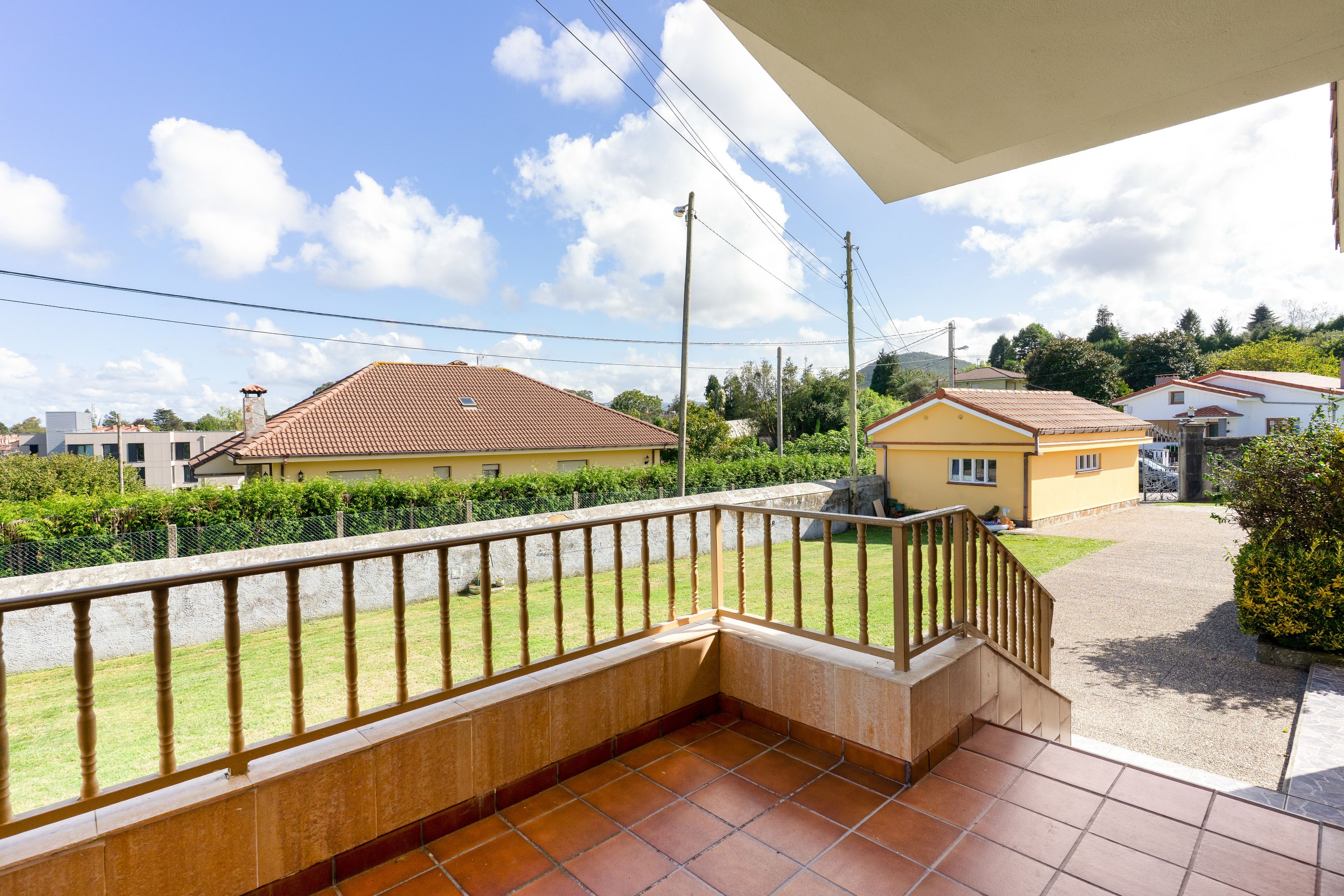 Un balcón con suelo de baldosas y baranda de madera, con vistas a una zona residencial con casas y cielo despejado.