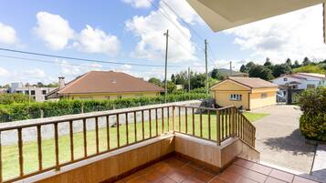 Un balcón con suelo de baldosas y baranda de madera, con vistas a una zona residencial con casas y cielo despejado.