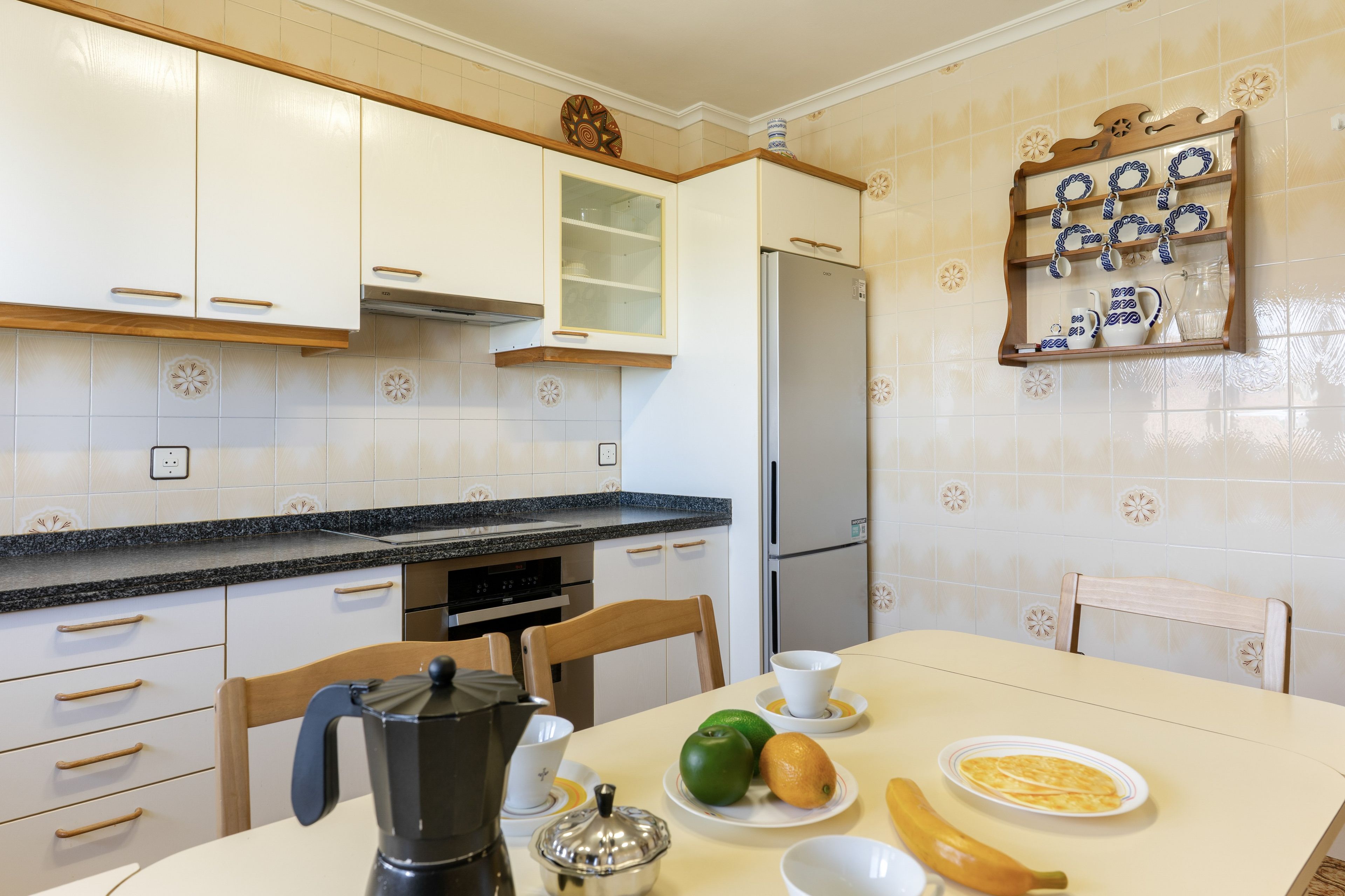 Una cocina con gabinetes blancos, encimera negra y refrigerador.
