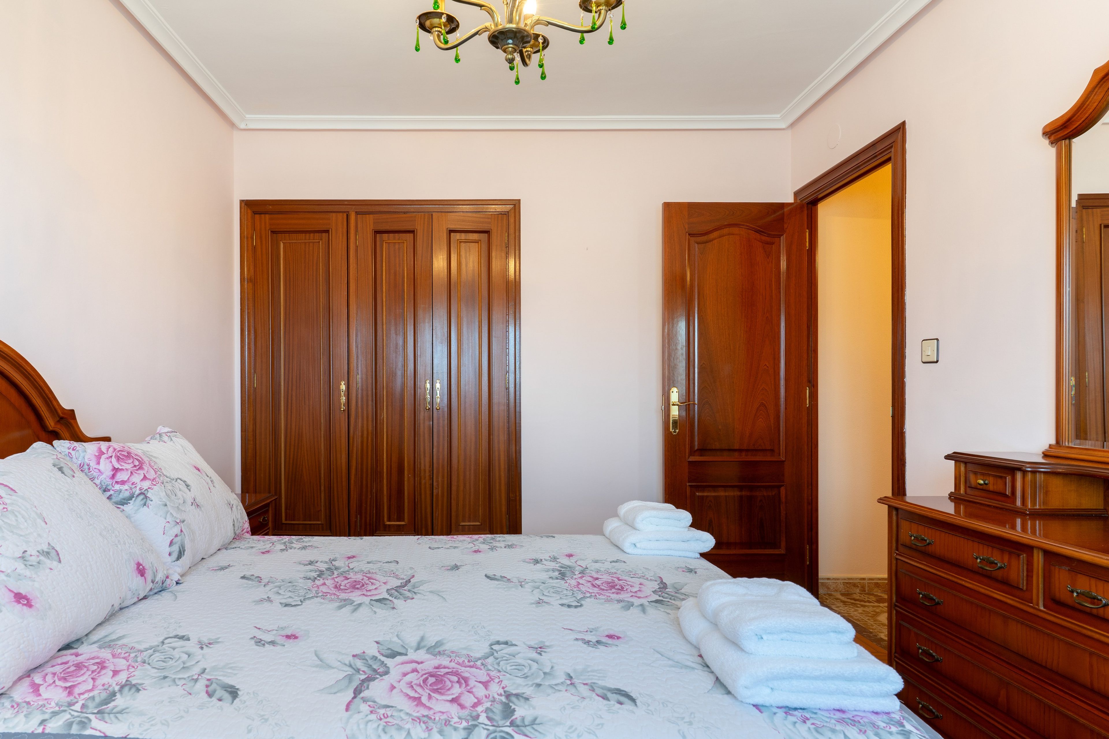 Un dormitorio con una cama, un armario de madera, un espejo y una araña.