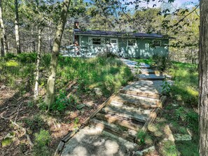Ein rustikales Blockhaus, verbunden durch einen Steinweg, umgeben von dichtem Wald.