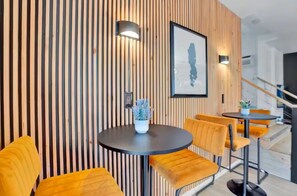 A modern interior with vertical wooden slats, round tables with yellow chairs, a potted plant, and a framed artwork on the wall. - Secluded Poconos Modern Cabin - Hot Tub, Game Room, Pools & Lake! (Big Bass Lake)