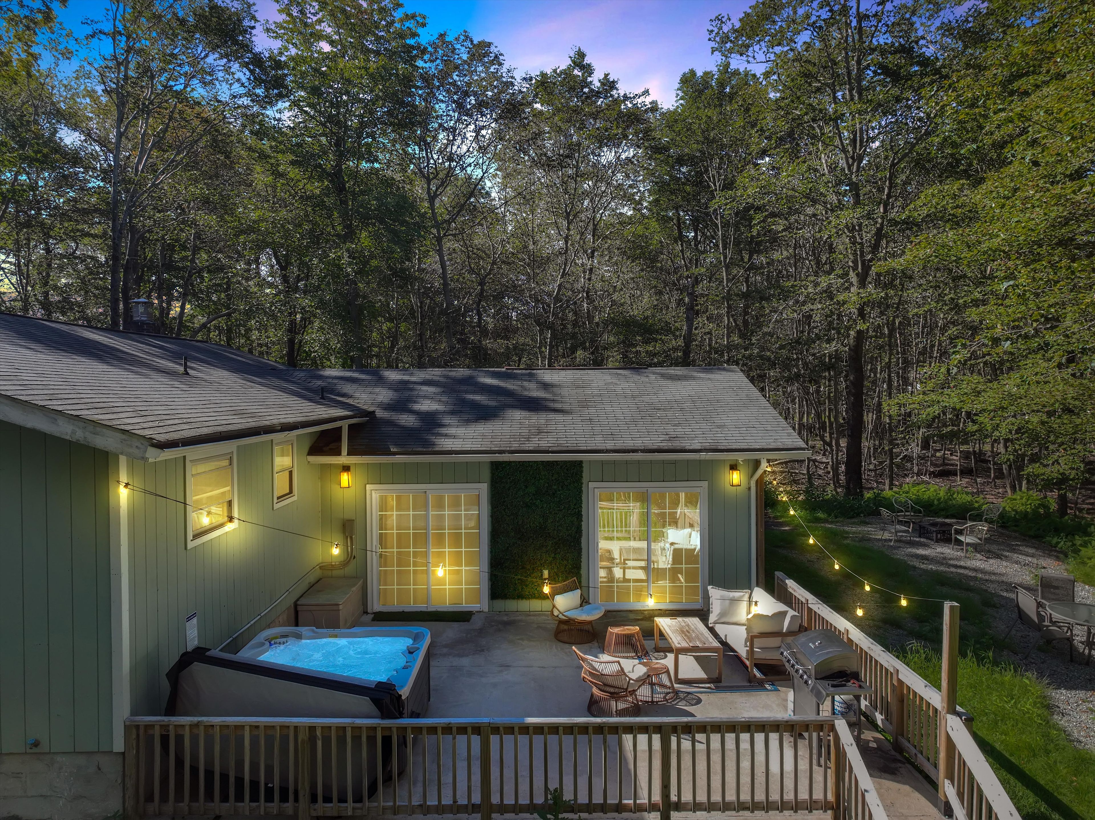 Ein Haus mit Whirlpool, Sitzgelegenheiten im Freien und einer Terrasse mit Blick auf einen Wald.