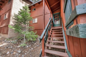A wooden staircase leading to a door with a window, surrounded by a small tree and a stone-paved ground. - Steps to Heavenly Mountain | Hot Tub & Fireplace (South Lake Tahoe)