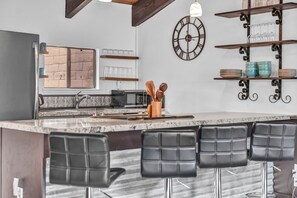 A modern kitchen with a bar area, featuring a marble countertop, black bar stools, and a decorative clock. - Steps to Heavenly Mountain | Hot Tub & Fireplace (South Lake Tahoe)