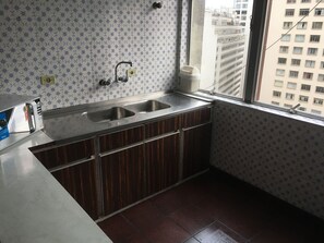 A kitchen with a double sink, wooden cabinets, and a window with a view of buildings. - Grande Apartamento no centro de Curitiba (Curitiba)