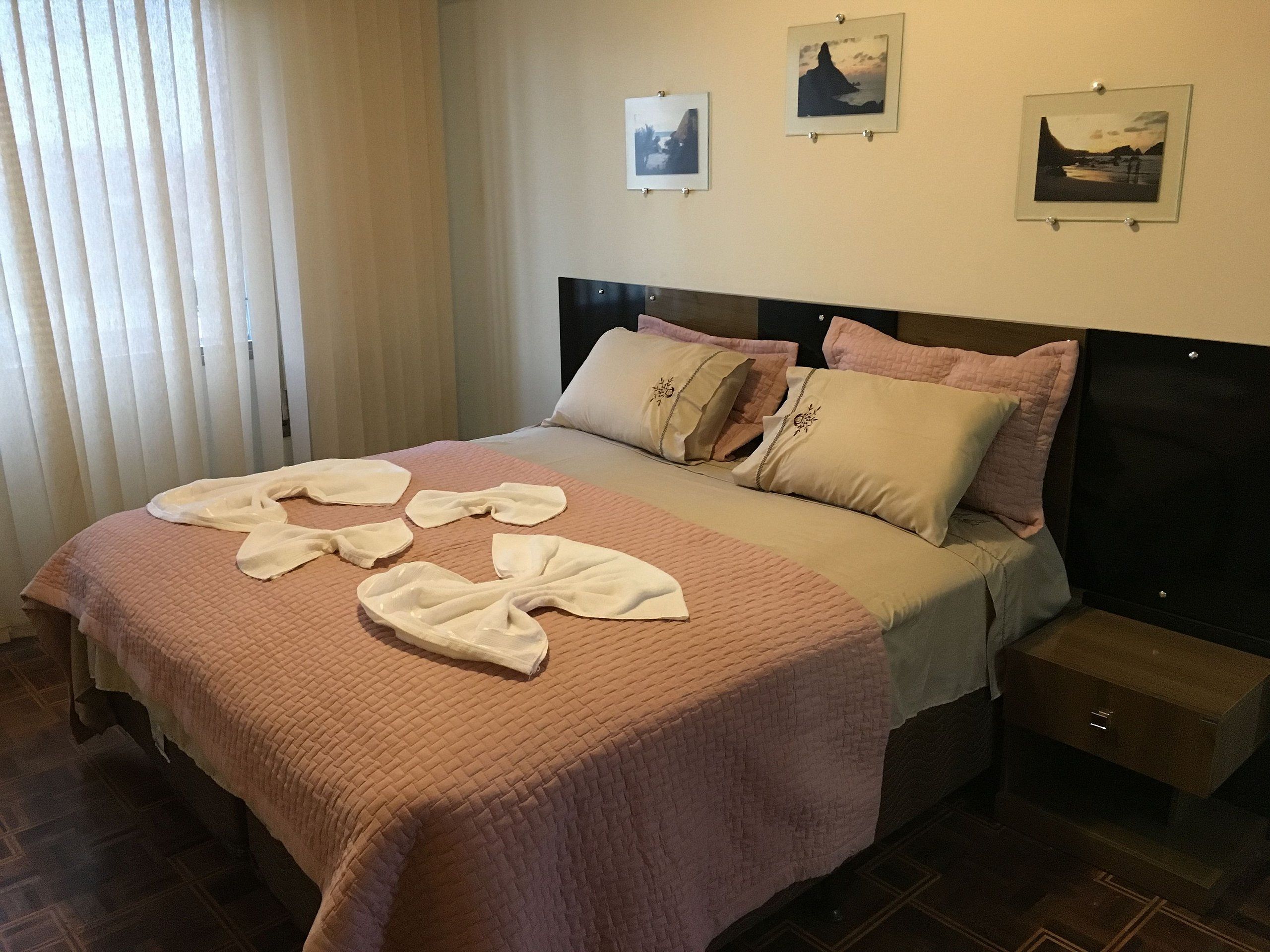 Habitación de hotel con cama, almohadas, mesita de noche y pared decorada con cuadros.