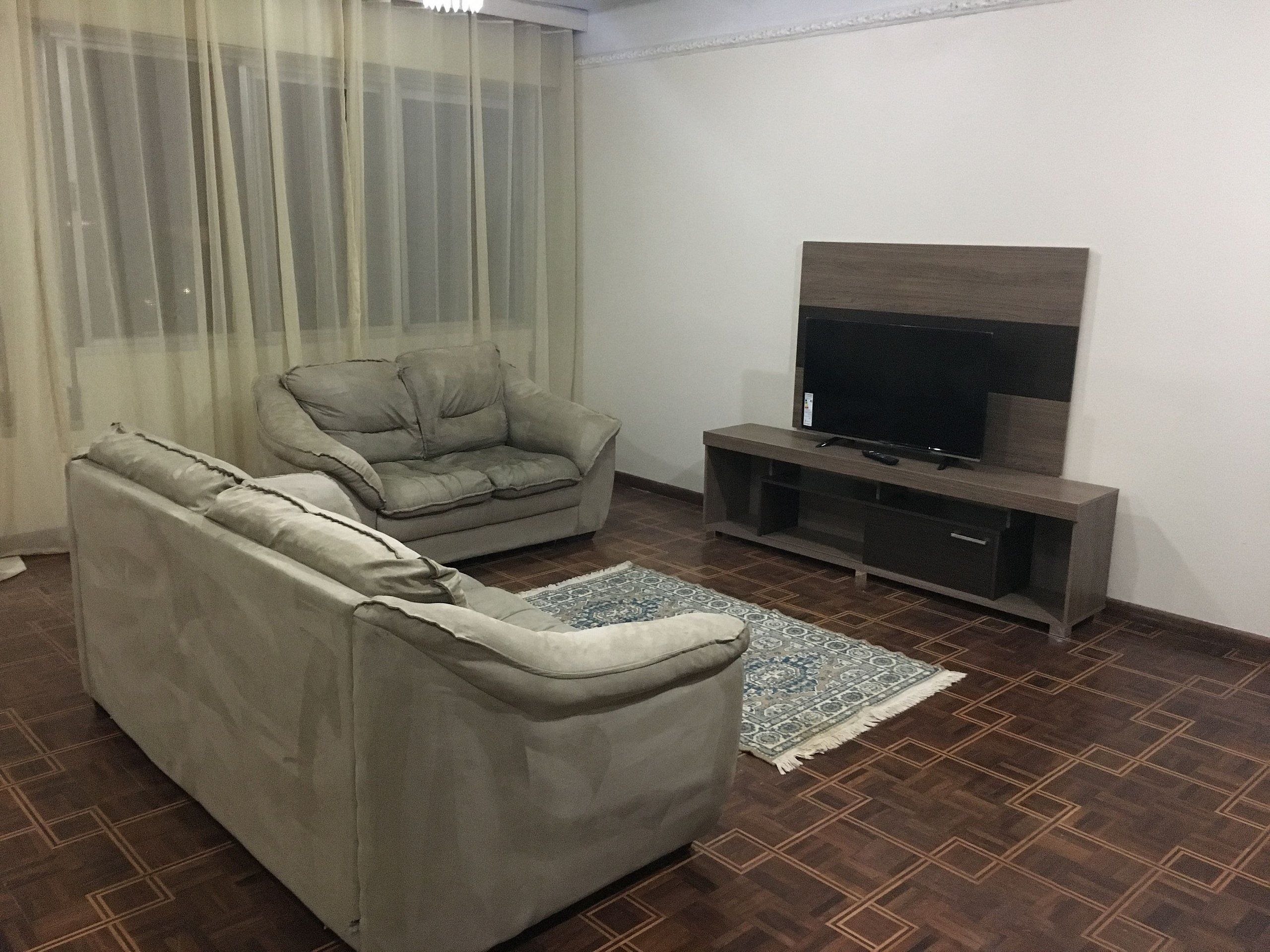 Una sala de estar con un sofá, un televisor sobre un mueble bajo y una alfombra estampada.
